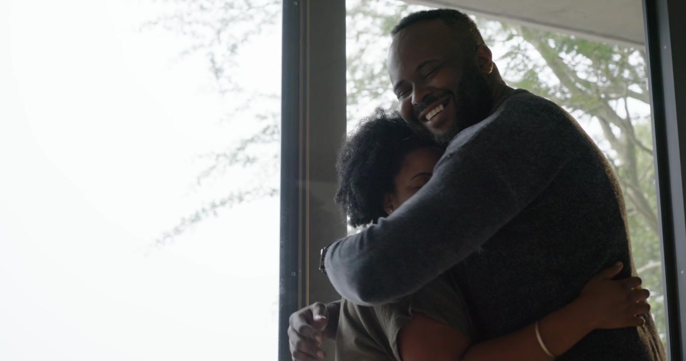 African American couple, woman reaching, hugging by glass doors expressing affection, copy space