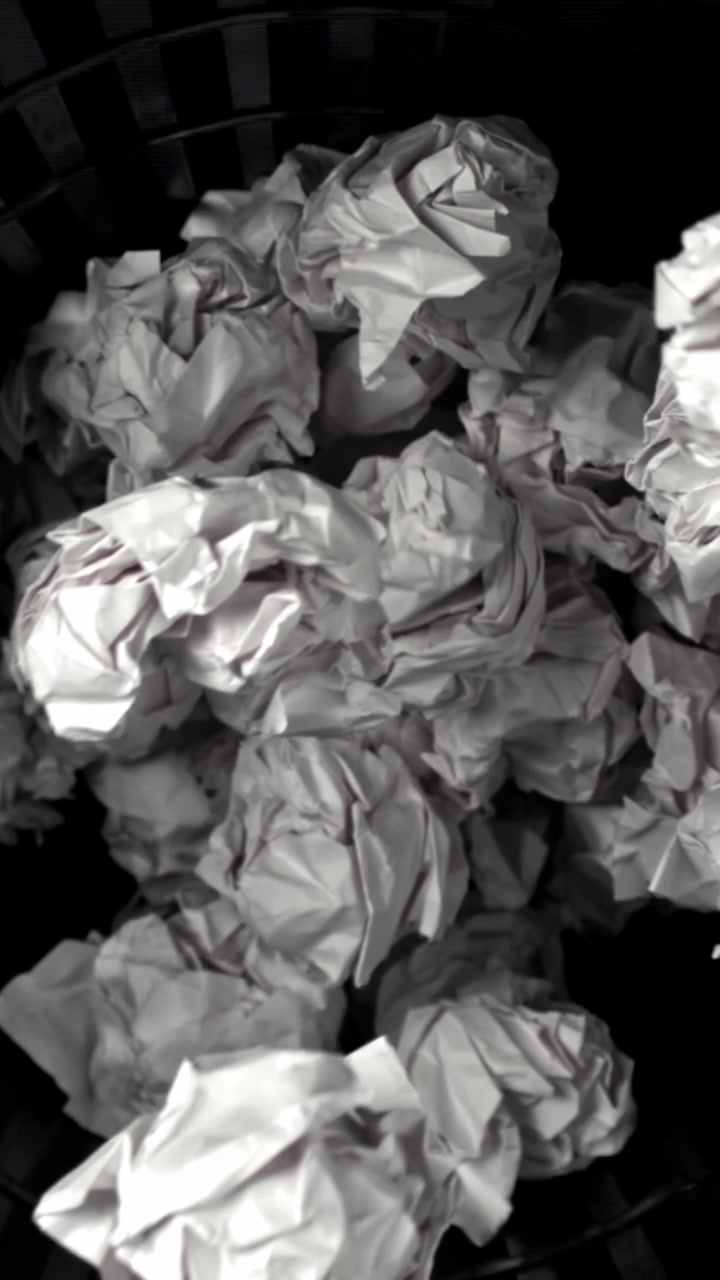 Crumpled White Paper Balls Falling into a Black Trash Can
