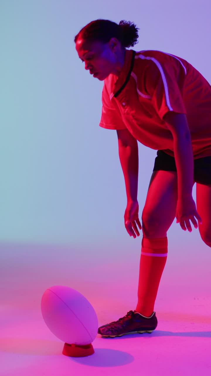 Neon pembe aydınlatma altında topla çömelen Afrikalı Amerikalı kadın ragbi oyuncusunun dikey videosu
