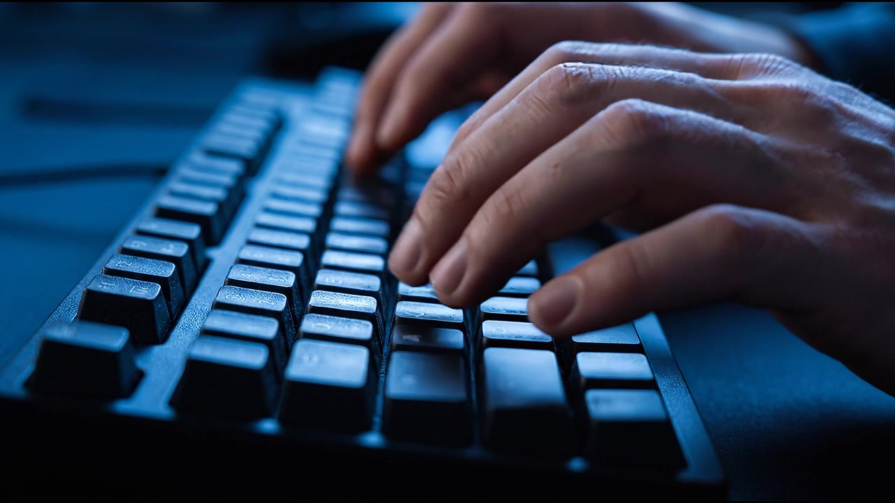 Close up of hands typing on illuminated mechanical keyboard during nighttime programming and gaming session