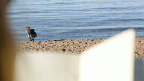 boy at the water playing with wooden stick mother reading