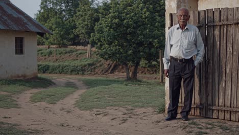 experienced educator standing near weathered wooden gate, rural schoolyard bathed in golden sunlight, symbolizing commitment to teaching in remote educational settings