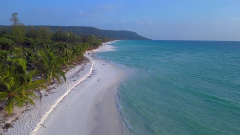 a pristine beach with palm trees meeting the crystal clear turquoise water on koh rong island, cambodia. lovely aerial view flight descending drone