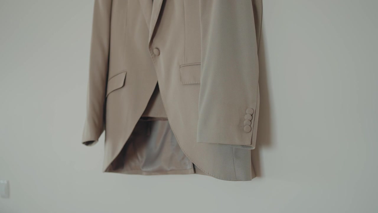 Giacca da completo beige chiaro appesa al muro con sfondo pulito e minimale.