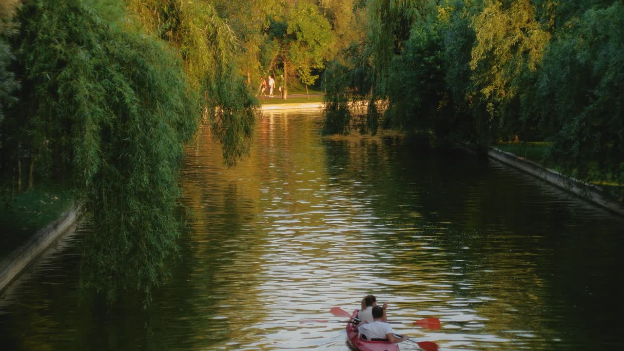 замедленная съемка пары в красном каяке на городском озере на закате с деревьями по берегам
