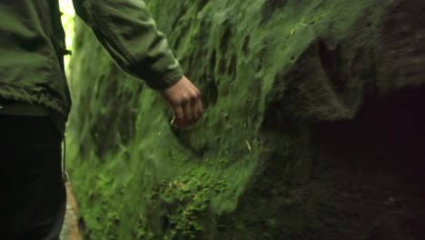 hand of a man touches and slides over stones with green moss in a canyon in nature close up tracking shot