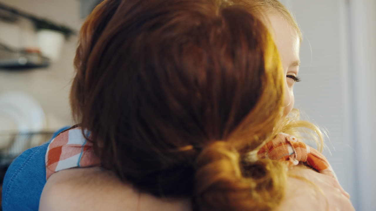 귀여운 금발 소녀가 엄마를 단단히 포옹하고 미소 짓는 장면. 엄마의 뒷면. 초상화 촬영. 실내