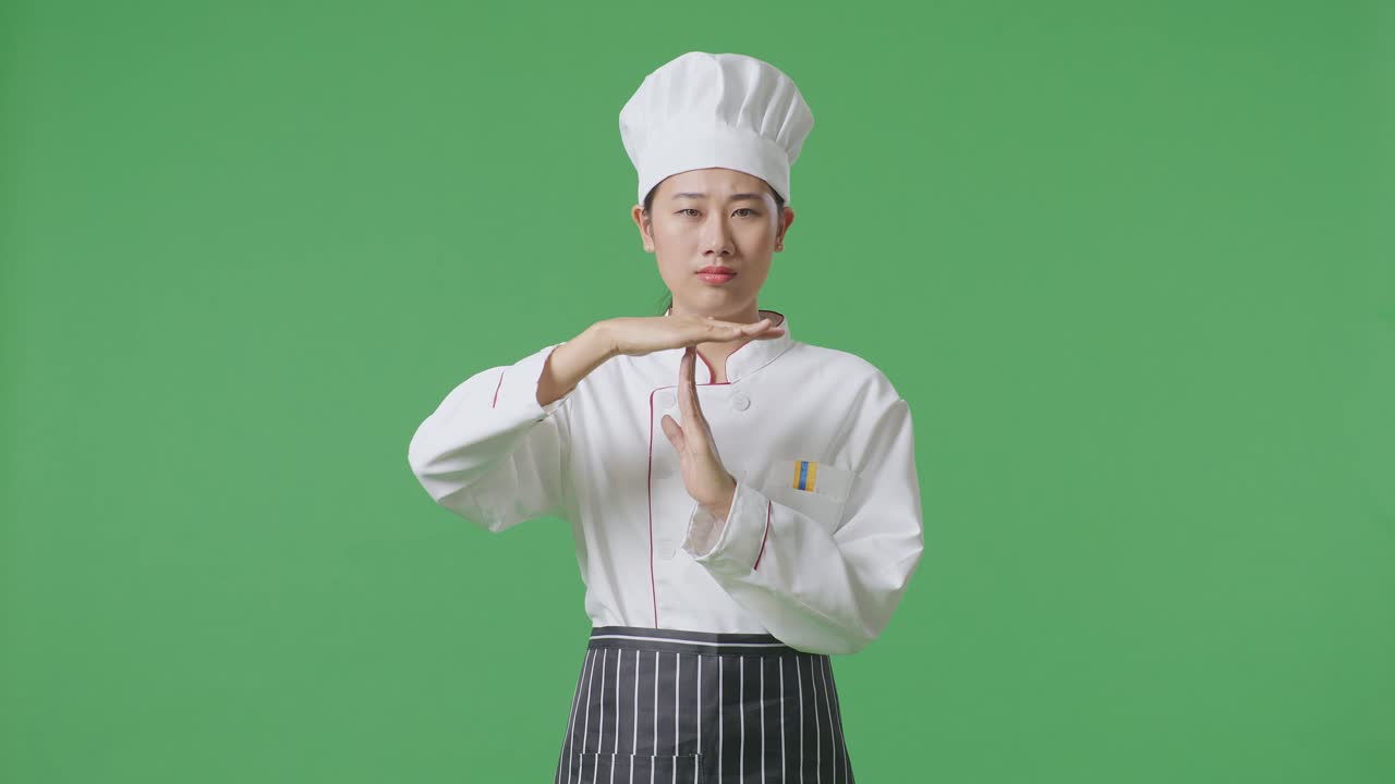 Asian Woman Chef Looking At Camera And Showing Time Out Hands Gesture While Standing In The Green Screen Background Studio
