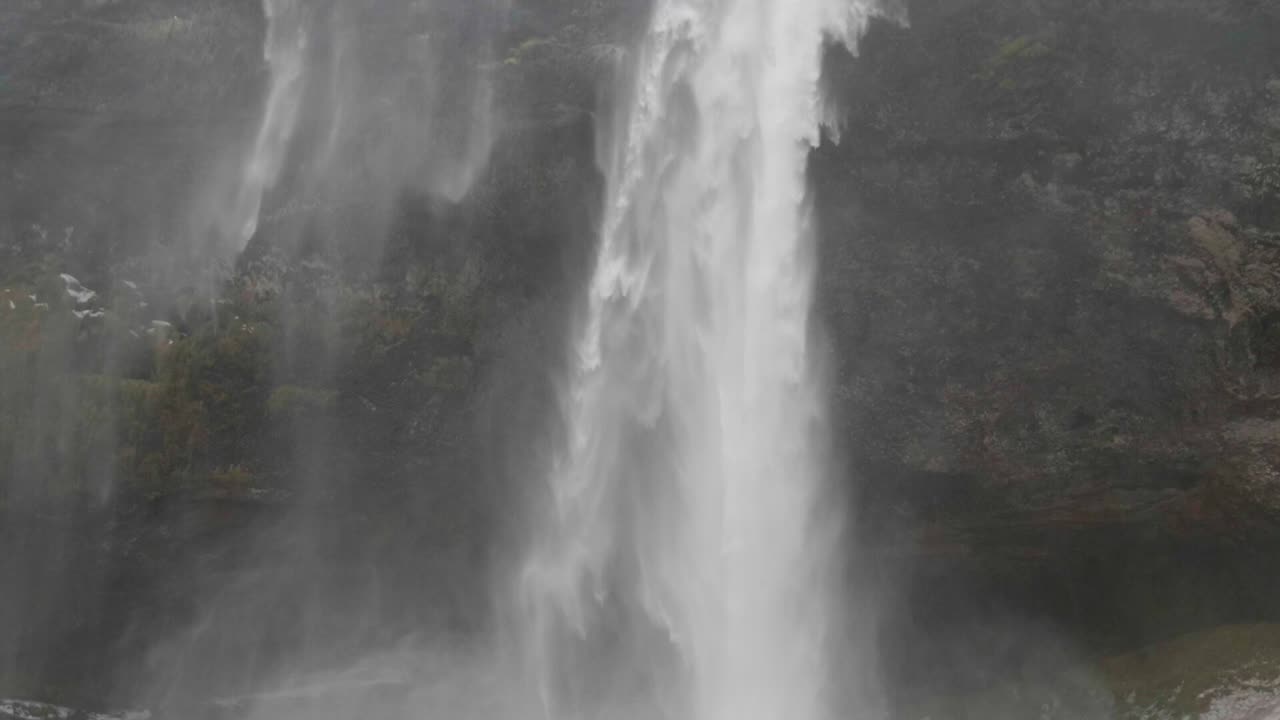 estático, cámara lenta, tiro inclinado, de agua que cae sobre suelo nevado, en la cascada de seljalandfoss, en un día nublado de otoño, en la costa sur, en la costa sur, de islandia