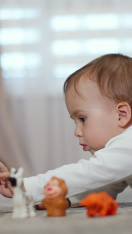 little caucasian boy lies on belly on the floor indoors. cute baby stretching arm to reach a toy car in front of him. blurred backdrop. vertical video