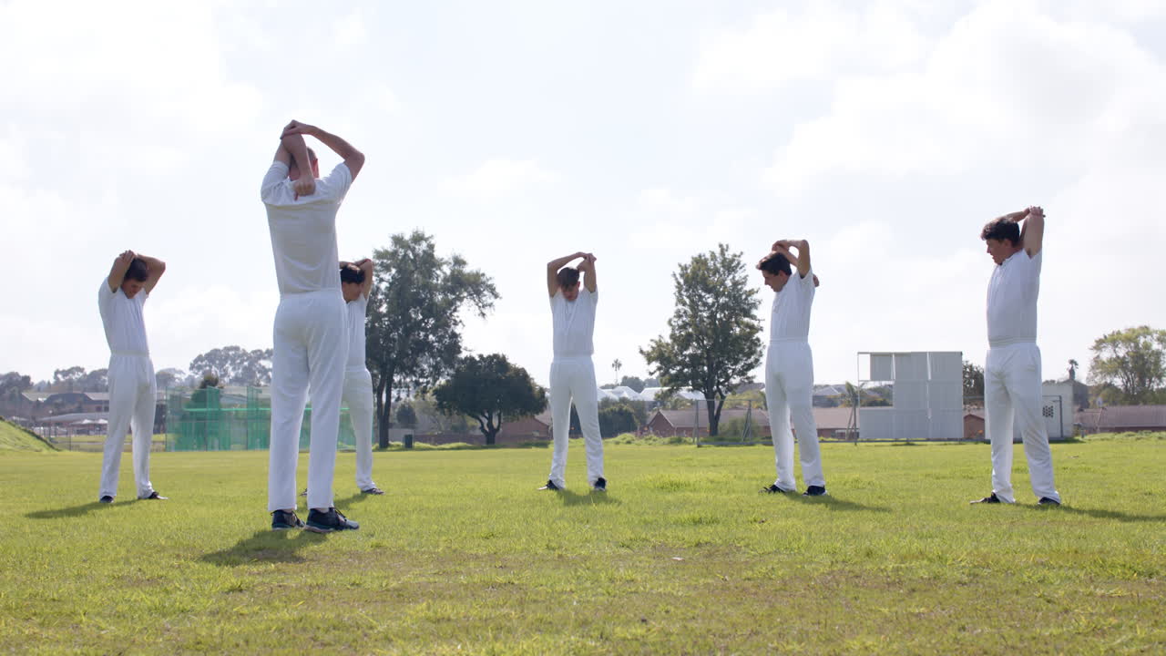 Team of male cricket players practicing cricket wearing cricket whites on pitch