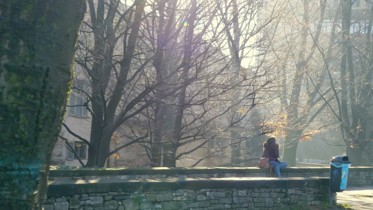 오래된 벽에 앉아 있는 젊은 여성은 아름다운 공원을 보면서 사과를 먹는다