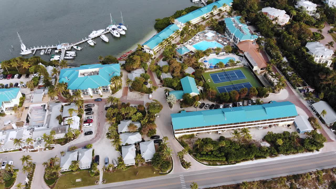 una toma diurna de un dron de un resort de una isla tropical con canchas de tenis, vías fluviales y botes visibles