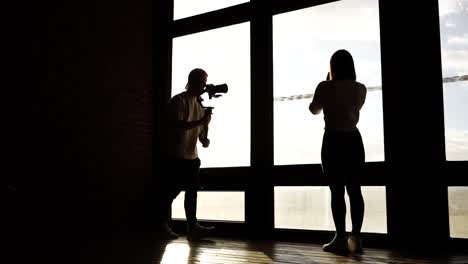 female model near bright window and videographer approach with camera