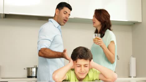 un niño molesto cubriéndose las orejas mientras sus padres pelean