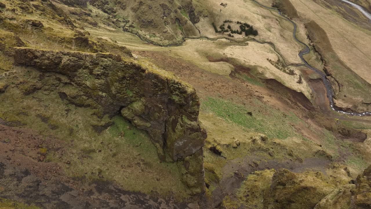 una impresionante fotografía aérea de un acantilado escarpado y cubierto de musgo en islandia, rodeado de tierra estéril y ríos sinuosos