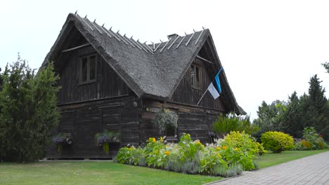 traditional wooden building in saaremaa estonia with a estonian flag waving on the house in slow motion during summer time while the weather is cloudy