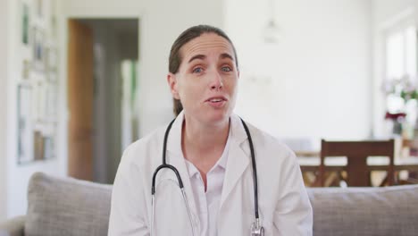 Happy-caucasian-female-doctor-sitting-on-sofa-having-video-call