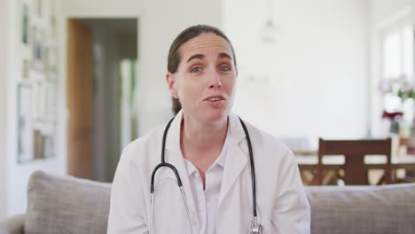 feliz doctora caucásica sentada en el sofá haciendo una videollamada
