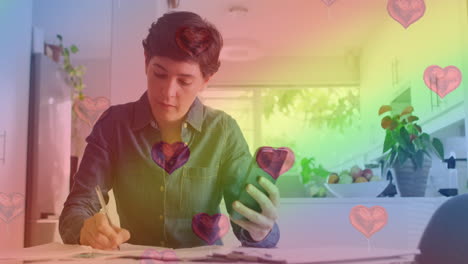 animación de emojis de corazón y bandera arco iris sobre mujer caucásica usando teléfono inteligente.