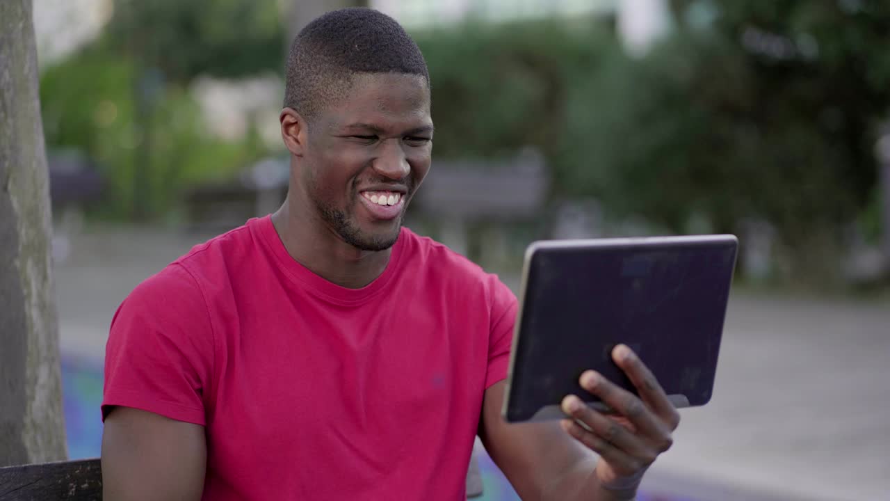 Man watching football match on tablet in park, celebrating goal
