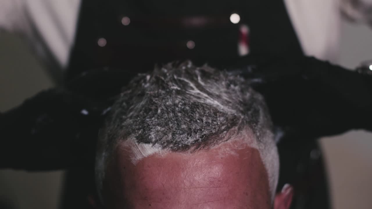 teñir el cabello del hombre aplicando el tinte con los dedos por un peluquero profesional