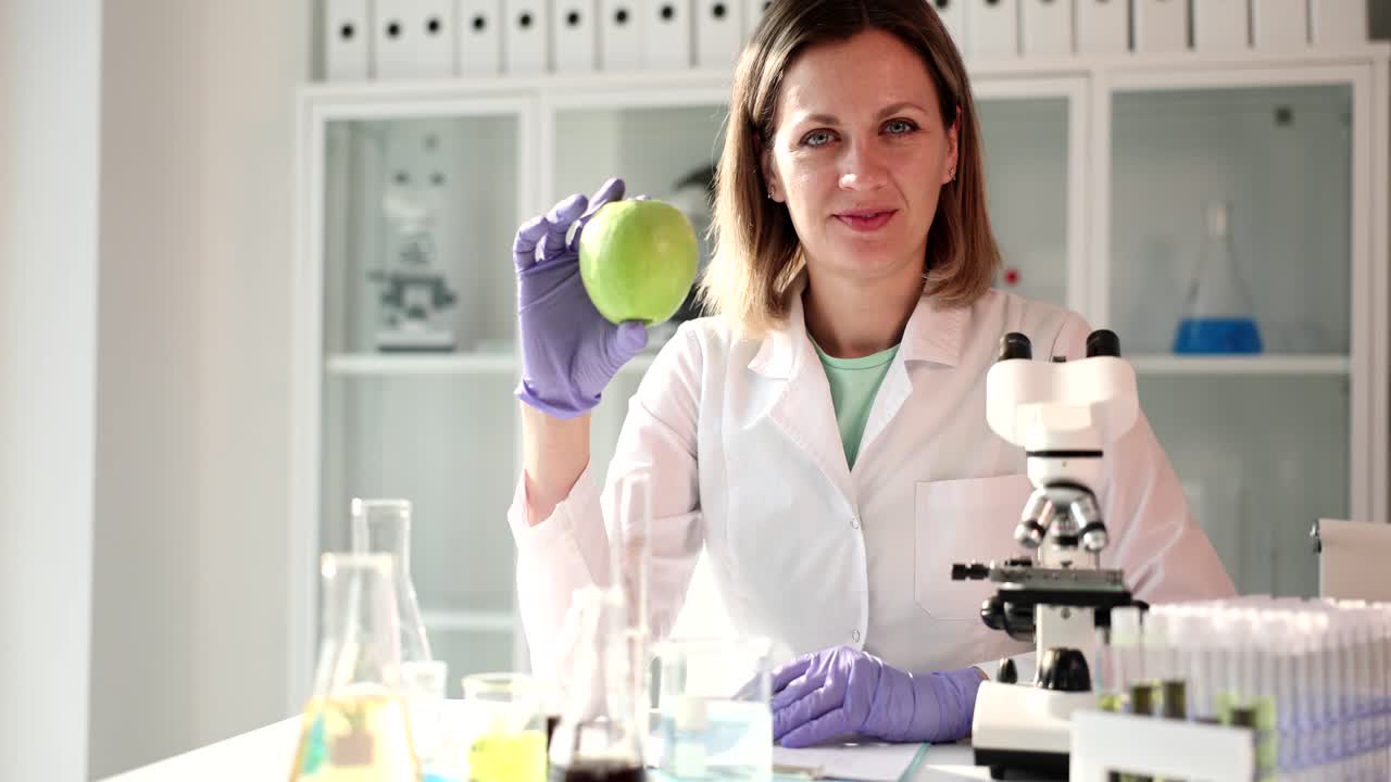 Female scientist in lab coat holding a green apple in a laboratory