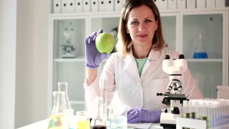 female scientist in lab coat holding a green apple in a laboratory