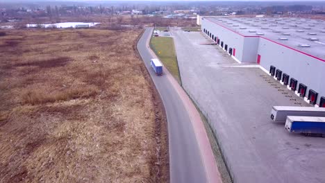 Buildings-of-logistics-center,-warehouses-in-the-field-near-the-highway,-view-from-a-height,-trucks-near-the-warehouse