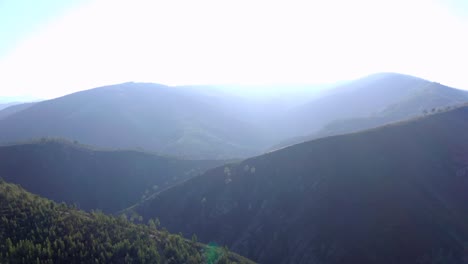 Una-Toma-A-Vista-De-Pájaro-De-Montañas-Y-árboles-Que-Van-En-Dirección-Al-Sol