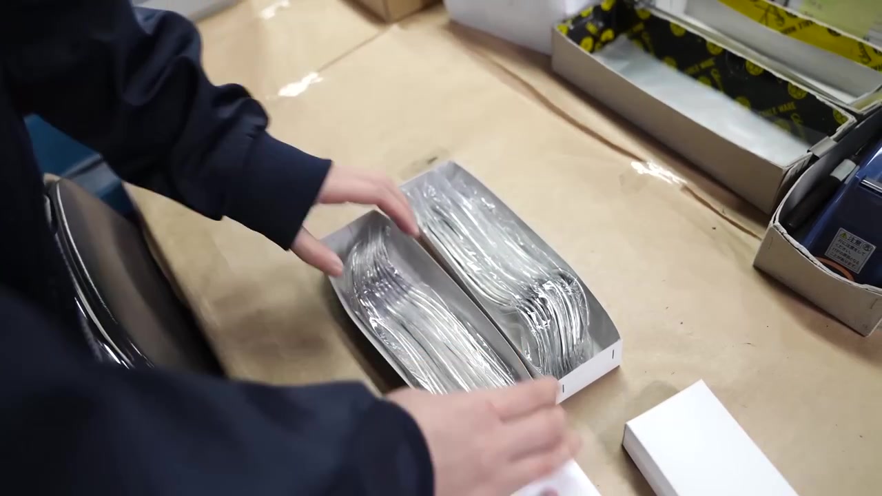 Worker placing white retail boxes over plastic wrapped stacks of forks on packing table