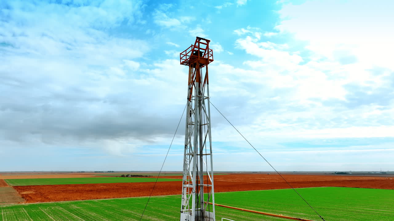 High tower in the field with the wires attached to it. Derrick for production of resources in the vast field.