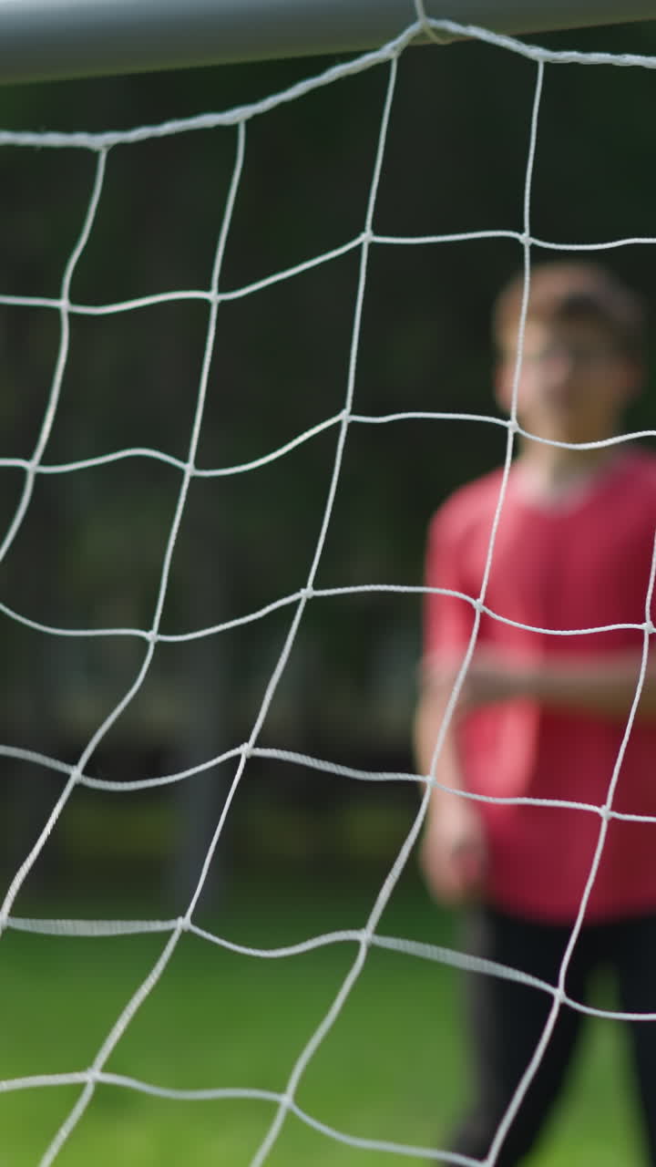 A close-up of a goal post captures the moment when a player in red shoots the ball into the net, and the goalkeeper misses the save, with the players clapping their hands in celebration