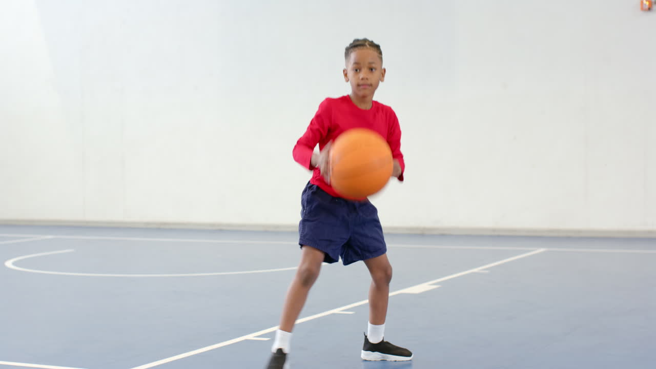 Boy practicing basketball skills on indoor court, focused and determined, copy space
