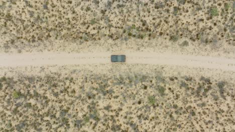 drone flies in bird's eye view over desert landscape in cederberg wilderness area in south africa over a road in the desert where a black off-road vehicle is driving