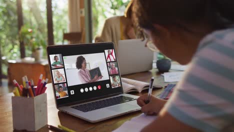 Girl-doing-homework-and-having-a-video-conference-with-teacher-and-classmates-on-laptop-at-home