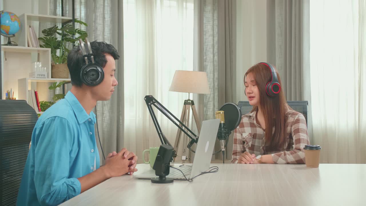 Young Asian Woman In Headphones Singing Into Microphone While Recording Podcast With Male Host In Studio