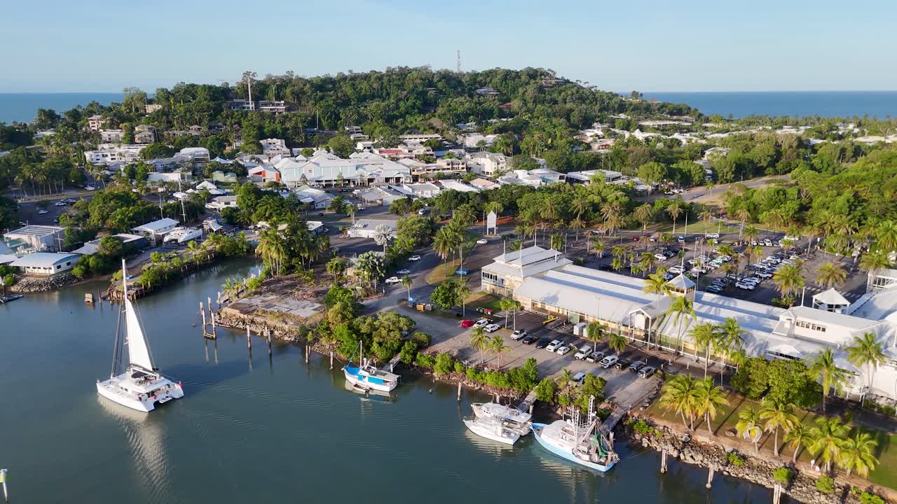 Drone footage captures Port Douglas marina and town with boats, lush greenery, and clear skies in a tropical setting