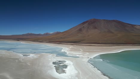 aerial drone rotating shot over partly frozen lake at the foothills of a mountain range in bolivia at daytime