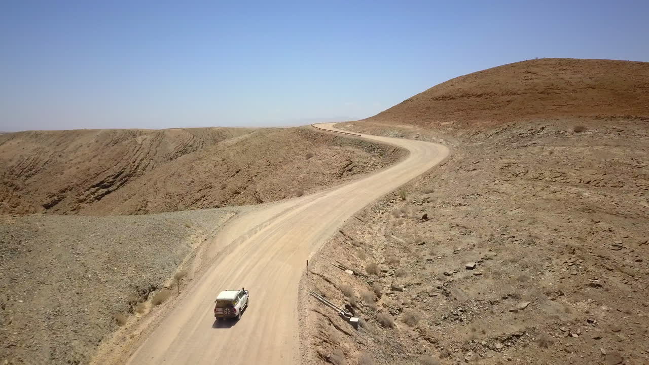 4K footage of a jeep driving along a dusty road in Namibia, captured from a drone following the vehicle. The breathtaking landscape and expansive views showcase the beauty of this African terrain.