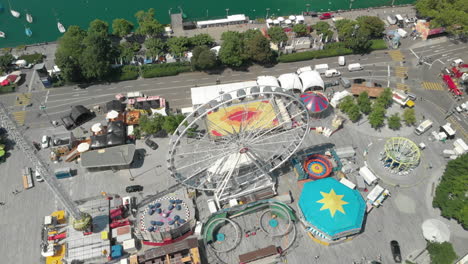 beautiful orbiting aerial drone shot flying down and around amusement park ferris wheel with the city of zürich, switzerland in the background during zürichfest