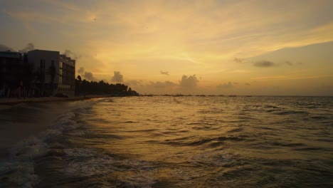 Drone-shot-zooming-forward-over-beach-and-water-off-Mexico's-coast-during-sunset