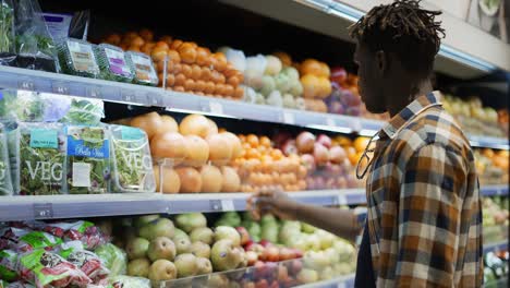 un tipo afroamericano eligiendo naranjas del pasillo de frutas.