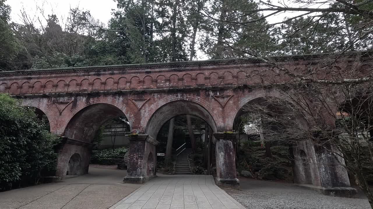 Red brick aqueduct arches through wooded grounds at Kyoto's Nanzen-ji Temple, blending Meiji-era engineering with natural beauty.