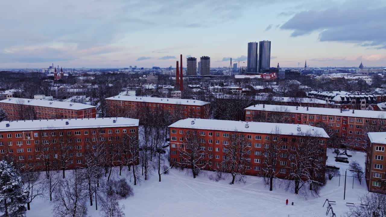 Panoramic drone shot reveals snowy Āgenskalns with Riga skyline in distance