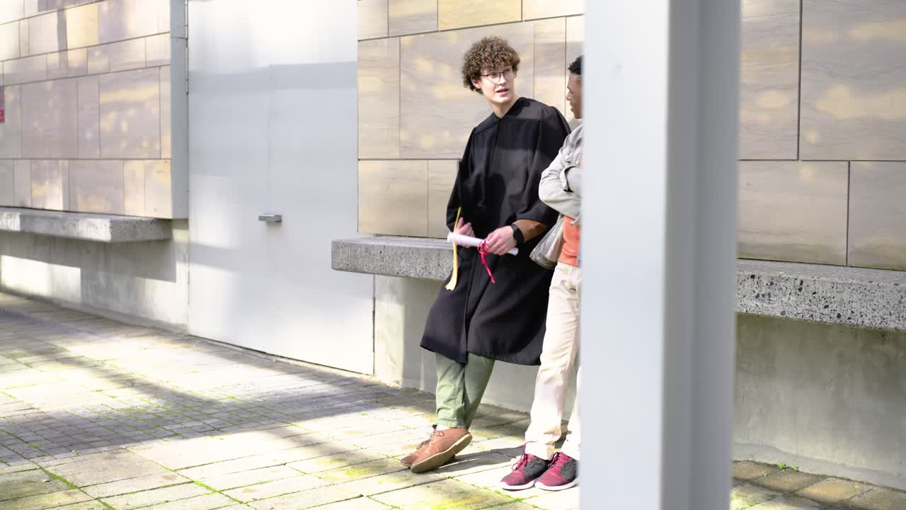 卒業後、キャンパスで寄りかかって話している成人男性2人。卒業生は角帽と卒業証書を手にしている