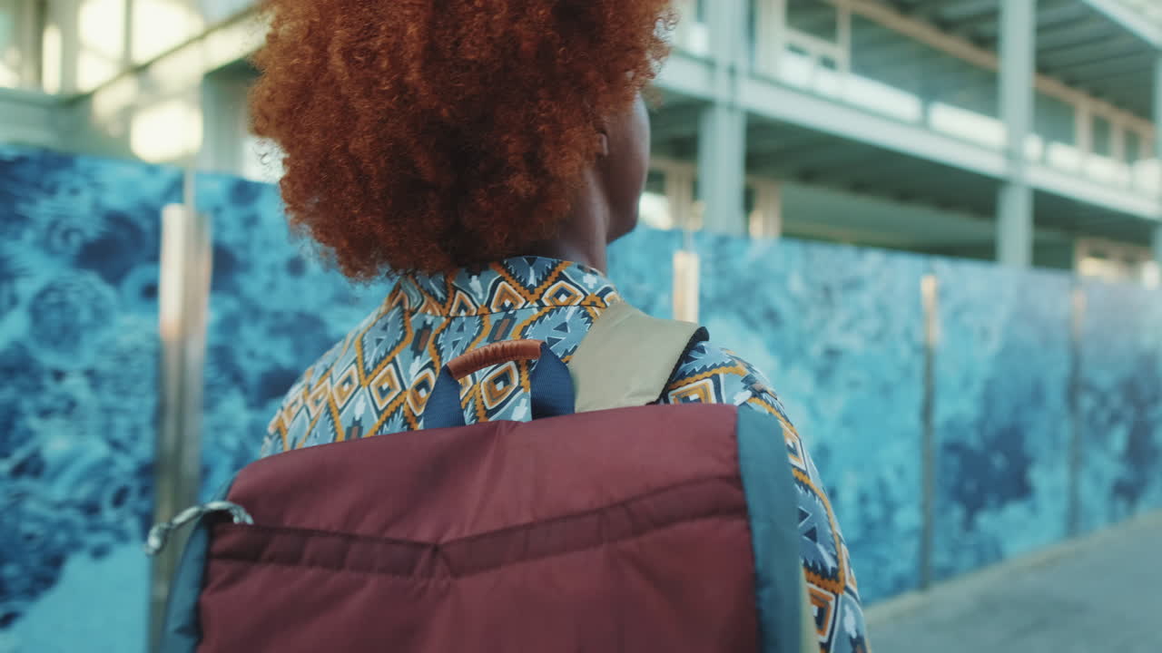 Person with Red Curly Hair Walking with Backpack Outdoors