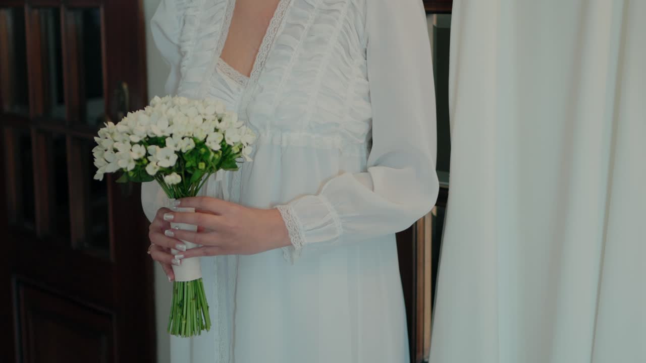 невеста в белом платье деликатно держит букет белых цветов, излучая простоту и грациозность