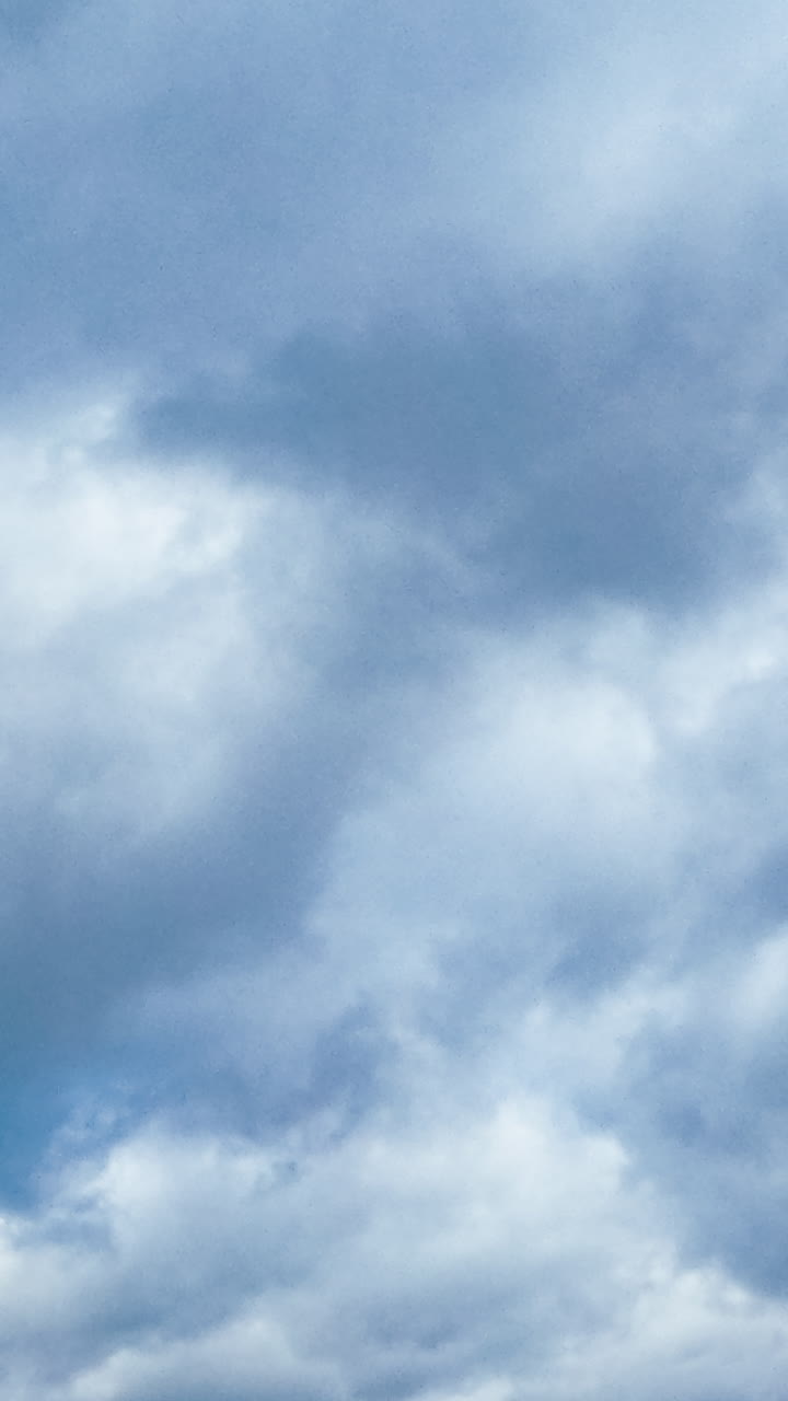 Fluffy grey clouds floating in the atmosphere. Overcast gloomy sky from low angle perspective. Vertical video
