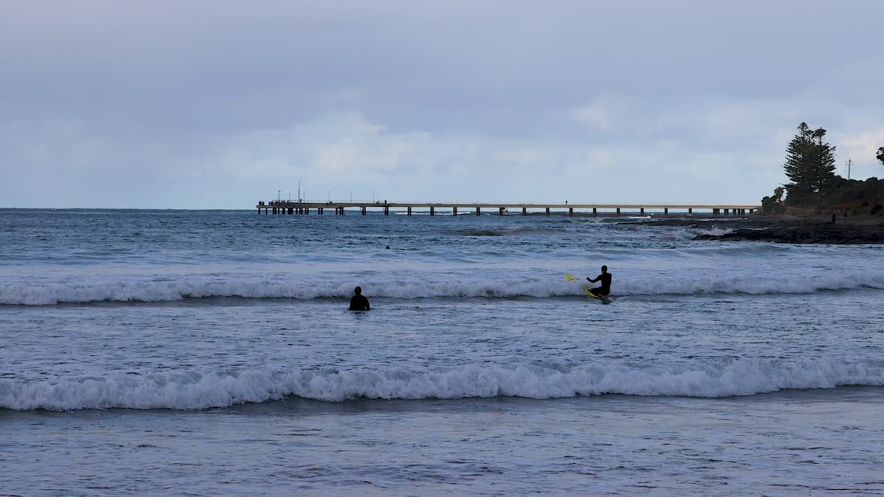 Surfers riding waves near a pier